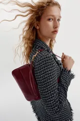 Bolso de hombro color bordó, con asa de hombro, bolsillo exterior con solapa y cierre de imán, y cierre principal con cremallera. Incluye detalle de anilla metálica dorada y tira con nudos en el lateral.