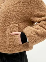 Campera negra de tela tipo sherpa con cierre frontal y cuello redondo.