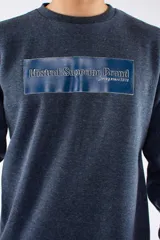 Buzo deportivo de cuello redondo en color azul marino jaspeado, con puños y ruedo acanalados. Presenta un estampado rectangular en el pecho con la inscripción 'Mistral Superior Brand'.
