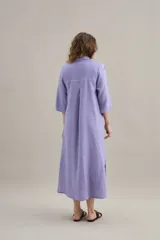 Vestido largo lila de lino, con cuello camisero, mangas cortas, bolsillos frontales con costuras a contratono y aberturas laterales.