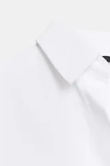 Camisa básica de algodón con cuello solapa, escote en pico y cierre frontal con botones. Presenta mangas largas con puños abotonados y bajo redondeado.