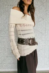 Jersey de punto color crema, con escote Bardot (hombros descubiertos) y manga larga acampanada. Presenta tejido calado con patrones horizontales y bajo festoneado.