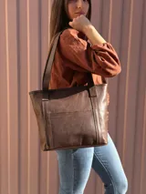 Cartera shopper de cuero color marrón chocolate, con doble asa de hombro, bolsillo frontal externo y diseño estructurado.