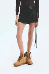 Minifalda negra de ecocuero con corte portafolio, tiro medio y lazos laterales ajustables.