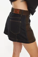 Minifalda de denim negro con costuras contrastantes en color ocre, pretina alta con trabillas y doble botón metálico.