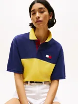 Chomba Tommy Hilfiger de corte amplio, con diseño color block en azul y amarillo, cuello clásico, cartera de tres botones, logo bordado en el pecho y logo oversize en la espalda.