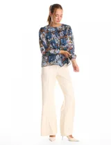 Blusa de gasa con estampado floral en tonos azules y marrones, con sutiles hilos de lurex dorados. Presenta cuello a la base, abertura central con botones, canesú delantero con pasamanería calada y mangas largas con puños elastizados. Incluye forro interno a tono.