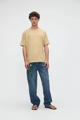 Remera de manga corta color beige, confeccionada en jersey de algodón con textura suave y calce relaxed. Presenta costuras a contratono en la espalda y un diseño estampado en la parte posterior con ilustraciones de estilo lineal y frases manuscritas.