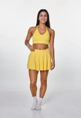 Conjunto deportivo compuesto por un top con cuello halter y una pollera short con diseño plisado, ambos en color amarillo.