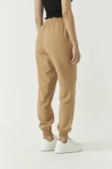 Pantalón de corte holgado confeccionado en mezcla de algodón y lino, color tostado. Presenta cintura elástica con cordón ajustable y puños elásticos en los tobillos.