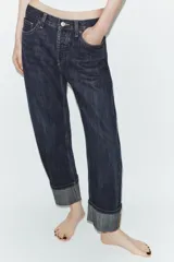 Pantalón de jean de tiro medio con corte recto y cinco bolsillos. Presenta un acabado con dobladillo ancho en el bajo y cierre frontal con botones metálicos.