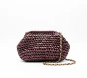 Bolso de mano artesanal con diseño anudado en color borravino, confeccionado con materiales reciclados. Cuenta con un interior forrado en seda y una cadena dorada desmontable como asa.