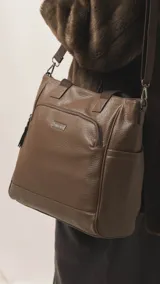 Cartera tipo tote marrón de diseño práctico y versátil, confeccionada en símil cuero con textura granulada. Cuenta con asas cortas fijas, bolsillos exteriores con cierre al frente y atrás, y bolsillos laterales abiertos. Su interior es amplio e incluye bolsillos organizadores. Viene con una correa ajustable y desmontable.