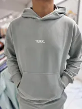 Conjunto de jogging celeste claro compuesto por un canguro con capucha y bolsillo tipo canguro con estampa pequeña del texto "TURK.", y un pantalón de jogging con puños elásticos en los tobillos.