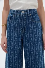Pantalón jean azul de tiro bajo y corte ancho, con estampado de rayas verticales y diseño floral sutil.