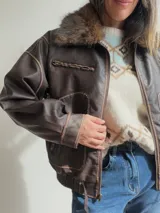 Campera estilo bomber de efecto cuero en color chocolate, con cuello de pelo sintético desmontable, cierre frontal, bolsillos laterales amplios y cintura elástica con ajuste lateral.