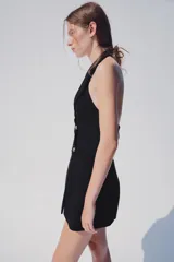 Mono negro de cuello halter con solapas, espalda descubierta y cierre frontal de botones con alamares.