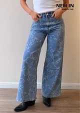 Jeans de corte wide leg y tiro alto, confeccionados en denim celeste con estampado de lazos en tono claro. Presentan cierre frontal con botón y cierre metálico, además de bolsillos funcionales.