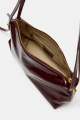 Bolso de hombro tipo baguette en color negro con acabado brillante. Presenta un diseño rectangular con cierre de cremallera superior y doble asa ajustable mediante hebillas metálicas.