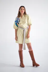 Vestido camisero corto color amarillo pálido con estampado floral en el hombro izquierdo y cinturón de tela con diseño geométrico.