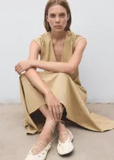 Vestido midi de corte evasé en color beige, con cuello en pico y manga corta. Presenta un diseño con costuras verticales decorativas y cierre de cremallera en la parte posterior.