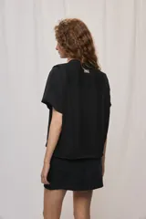 Camisa negra de manga corta, silueta amplia y tejido liviano con textura. Presenta cuello mao, cierre frontal con botones y diseño fluido.