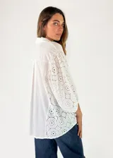 Camisa blanca con cuello camisero, cierre frontal de botones y mangas tres cuartos abullonadas con bordados suizos y detalles perforados en los laterales y mangas.