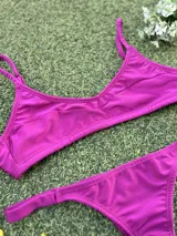 Conjunto de bikini color magenta con acabado metalizado. El corpiño es tipo top con breteles finos y la bombacha es de corte colaless.