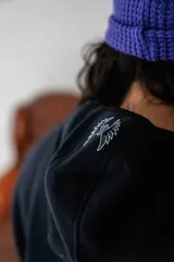 Canguro negro con capucha, cierre frontal parcial y bolsillo tipo canguro. Presenta un estampado gráfico pequeño en el centro del pecho.