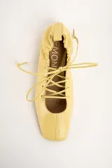 Chatitas de cuero color amarillo, con diseño acordonado en el empeine, puntera cuadrada y talón fruncido con cordón ajustable.