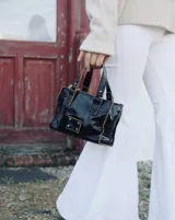 Mini bag negra de cuero charol con doble asa corta y detalles de costuras en color tostado.
