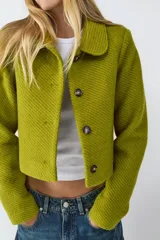 Campera corta de tejido piqué con textura marcada, cuello camisero y cierre frontal de botones. Presenta un calce estructurado y diseño moderno.