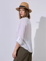 Camisa blanca de gasa con cuello a la base y escote en V, abertura central con botones, bolsillo aplicado en el pecho, mangas largas regulables con presilla y terminación anudada opcional.