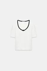Camiseta blanca de manga corta y corte slim fit, con escote redondo ribeteado en negro, detalle de frunce en el centro del pecho y un pequeño lazo negro decorativo.