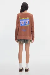 Buzo de felpa sin frisa color terracota con efecto washed, cuello redondo y fit relajado. Presenta un pequeño estampado azul en el pecho.