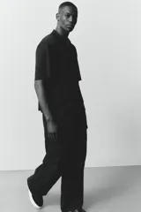 Pantalón cargo negro de corte holgado, con cintura elástica ajustable con cordón, bolsillos laterales al bies, bolsillos tipo cargo con solapa y botón a presión en las piernas y bolsillos traseros con solapa y botón a presión. Cuenta con pliegues cosidos en las rodillas y cordón ajustable oculto en el bajo.