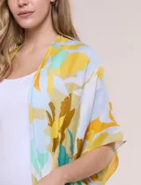Kimono de gasa ligera con estampado floral en tonos amarillos, celestes, blancos y marrones, de manga corta amplia y diseño abierto con detalle de borlas en el ruedo asimétrico.