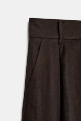 Pantalón de tiro alto y pernera ancha, color marrón, con pinzas delanteras, bolsillos frontales y cierre con cremallera y botón.