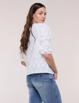 Blusa blanca de calce holgado, con bordado en relieve tipo broderie de motivos florales en toda la prenda. Presenta escote en V con fruncido en los hombros, cierre frontal con botonadura y mangas tres cuartos abullonadas con puños elastizados.