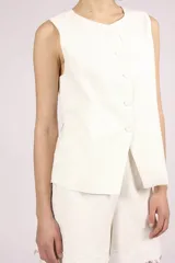 Chaleco blanco sin mangas, con cuello redondo y cierre frontal de botones. El chaleco tiene un corte recto y ligeramente holgado.