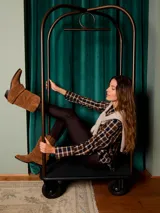 Bota de caña media confeccionada en gamuza color marrón, con diseño de pliegues naturales y caída suave. Presenta punta afinada y taco acuñado, con un estilo inspirado en la estética western.
