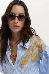 Camisa de algodón a rayas celestes y blancas, con mangas abullonadas y gran estampado floral en el frente.