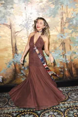 Vestido largo de encaje y transparencias color marrón, con escote profundo halter, frunces en el cuerpo, espalda abierta y tiras largas estampadas para atar al cuello.