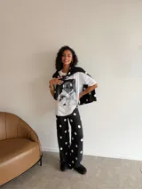 Conjunto compuesto por un remerón blanco de algodón con estampa frontal de un oso con auriculares y taza de café, y un pantalón negro de corte recto con estampado de lunares blancos.