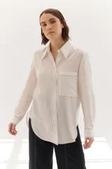 Camisa color crema de lyocell con cuello clásico, cierre frontal con botones, bolsillo de parche en el pecho y pespuntes a contraste en negro.