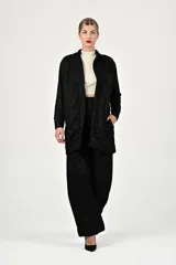 Conjunto de dos piezas en color negro con sutiles destellos brillantes. El saco es de corte recto, tipo cárdigan, con solapas y bolsillos frontales. El pantalón es de corte amplio y tiro alto.