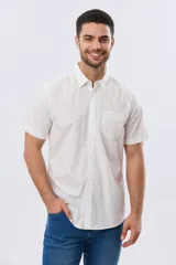 Camisa lisa de algodón azul marino, de manga corta, con cuello camisero, cierre frontal de botones y un bolsillo aplicado en el pecho.