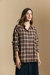 Camisa de estilo leñador con estampado de cuadros en tonos azul, negro y marrón. Presenta cuello clásico, cierre frontal con botones y mangas largas con puños abotonados.