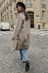 Abrigo largo cruzado color gris oscuro, confeccionado con lana. Presenta cuello solapa, manga larga, bolsillos delanteros de plastrón y cierre frontal con botones.