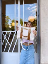 Bolso tipo tote de lona color crudo con detalles en cuero color marrón. Tiene doble asa corta de mano y correa larga de hombro.